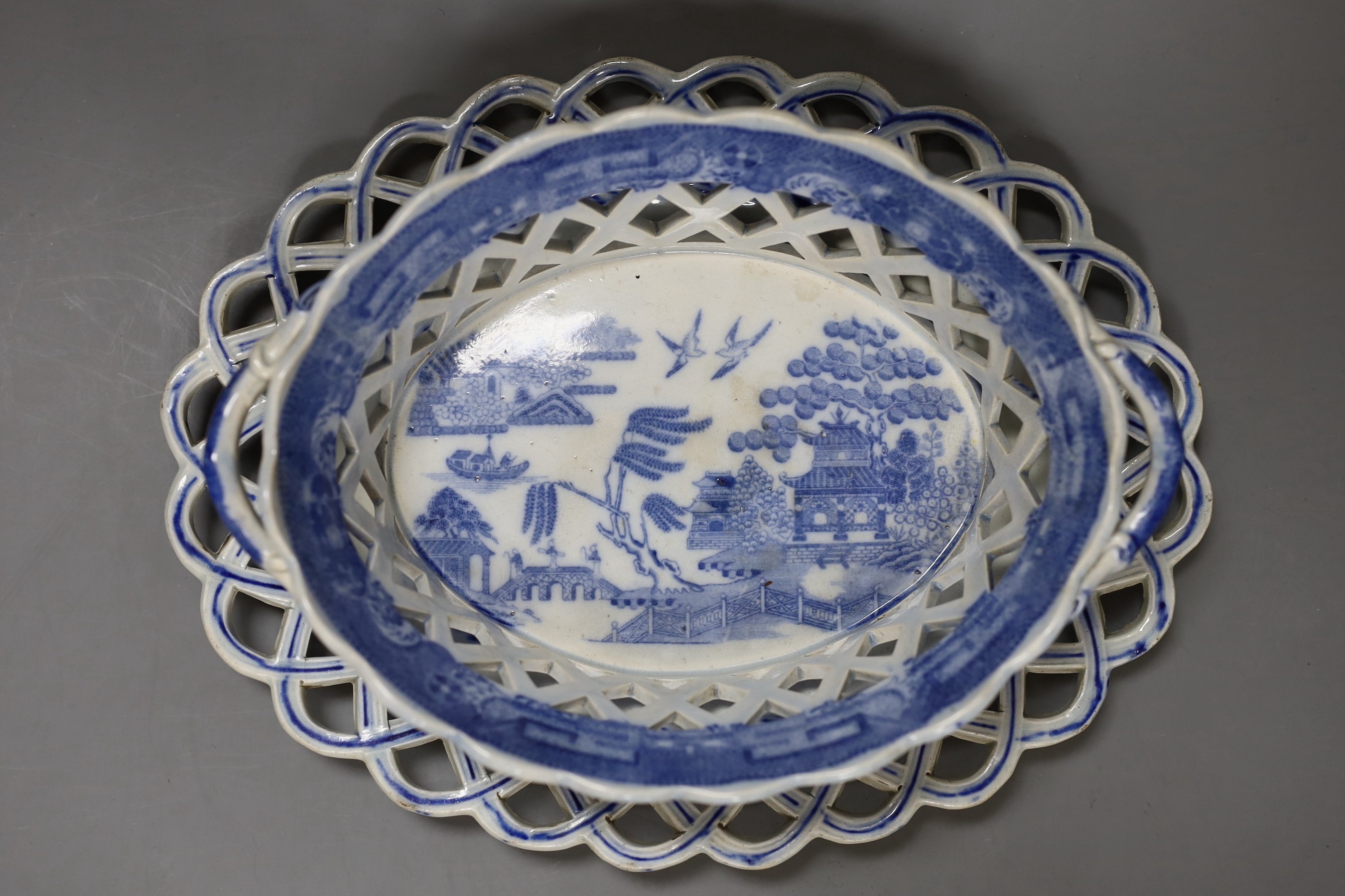 An early 19th century English blue and white pearl ware oval two handled chestnut reticulated basket with transfer printed chinoiserie decoration, together with a similar oval stand